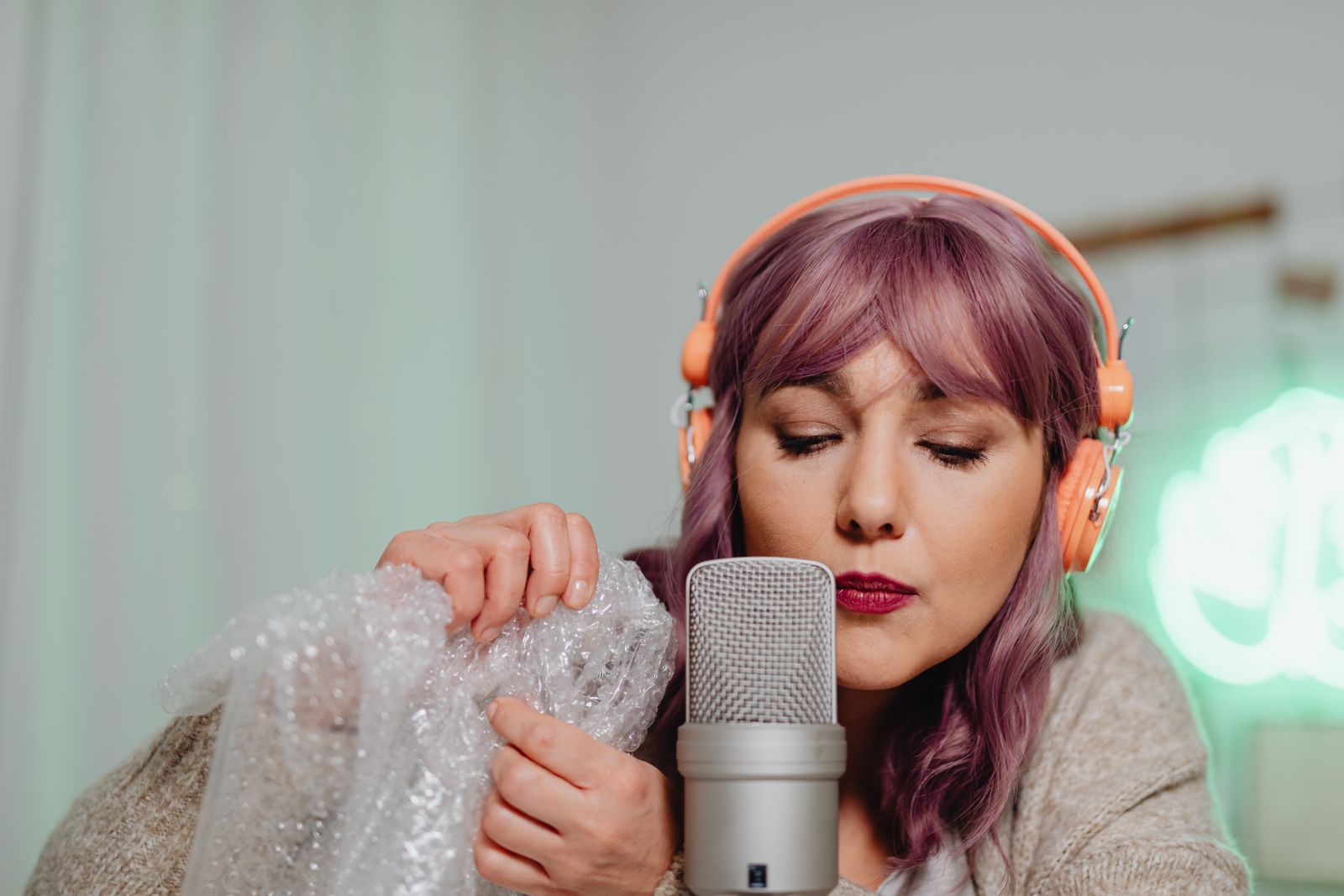 Apresentadora de cabelo colorido gravando em microfone de mesa com fones laranja